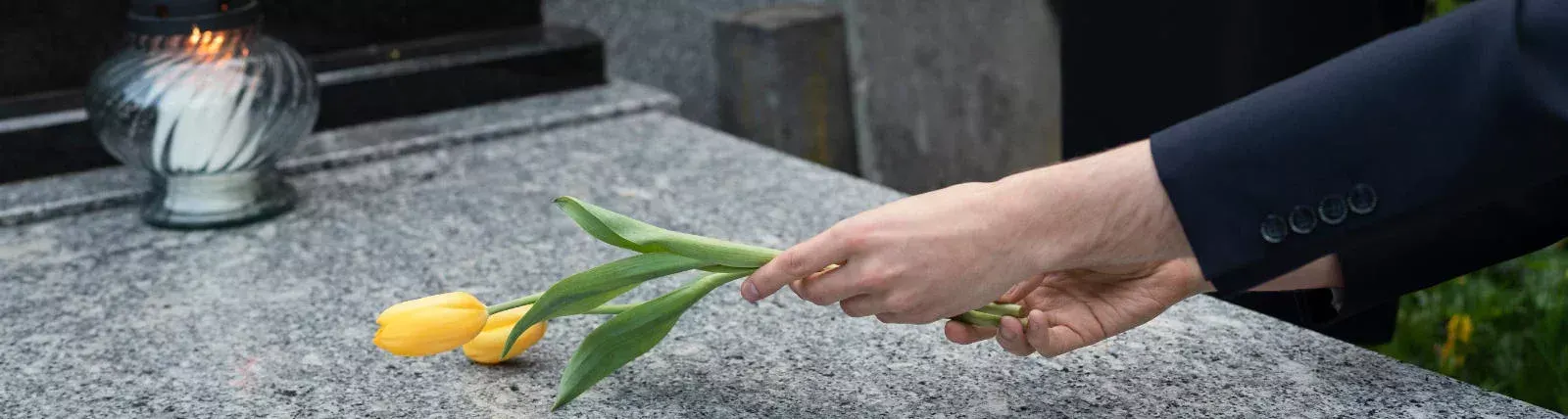 Ruka pokládající tulipány na žulový pomník — kamenictví Litrade Liberec